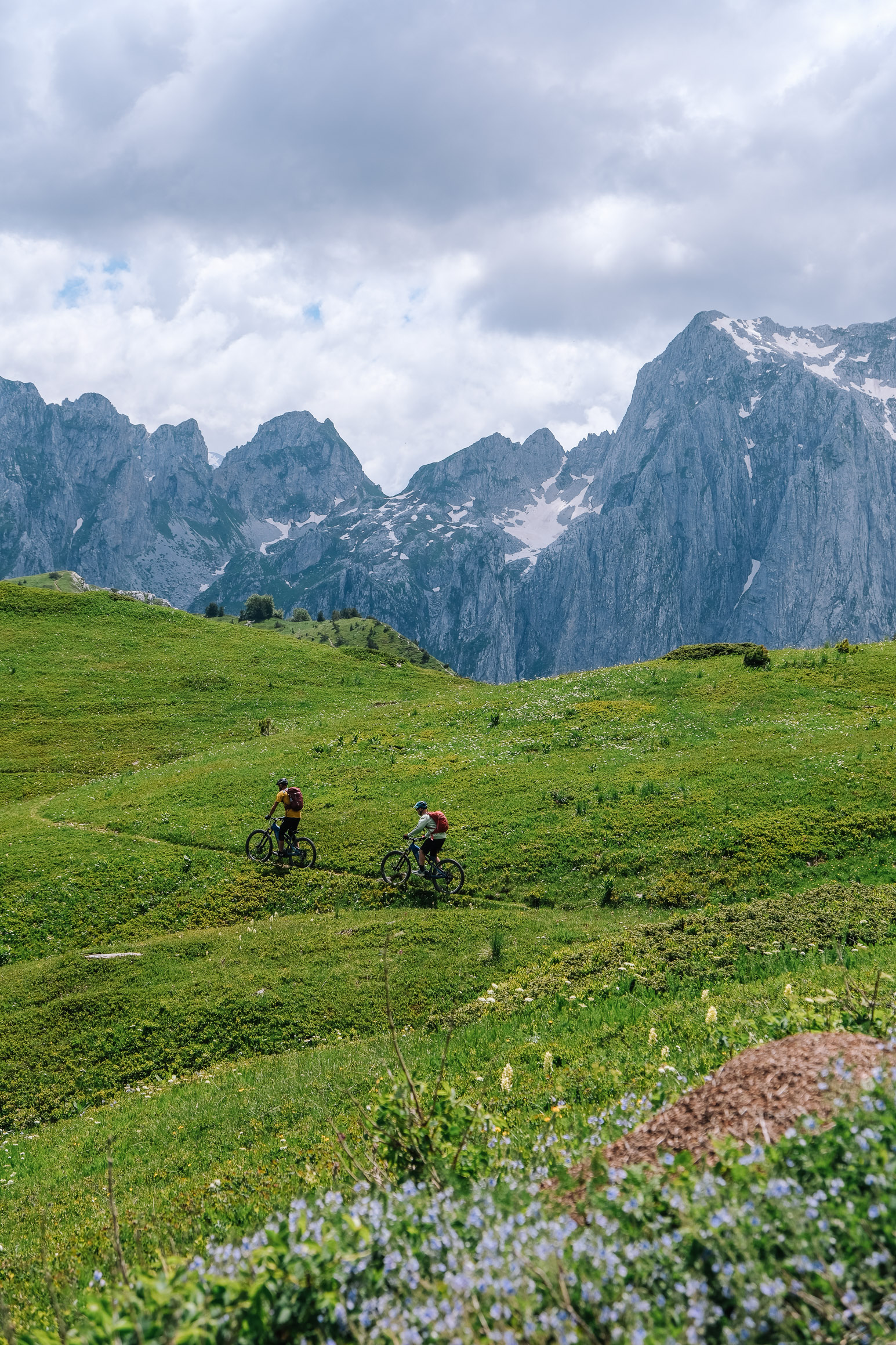 Riders crossing an alpine meadow below the jagged peaks above Gerbaja